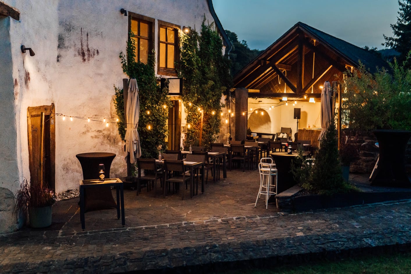 Murmure du Château's lantern-lit terrace at dusk, tables set beneath the old guard house